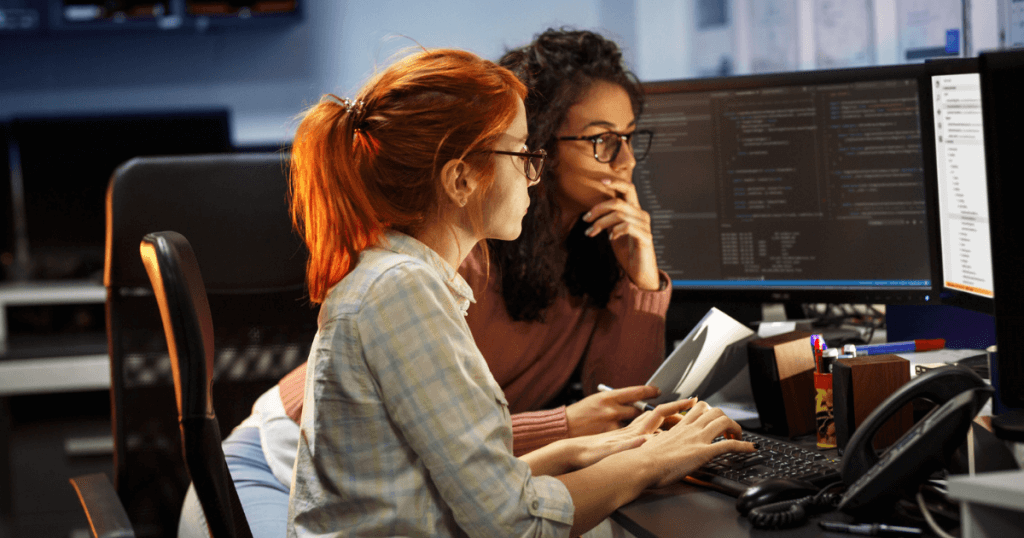 Two women working late at night. They are both looking at a computer screen and need advice to keep their eyes protected at work.